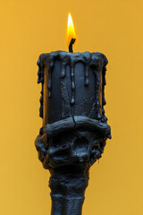 Poster - A skeleton hand holding a single black candle wick, set against a pastel yellow background,