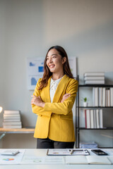 Wall Mural - young asian businesswoman smiling and standing with arms crossed in modern office