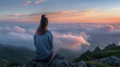 © NooPaew - Rear view of a young woman sitting on a mountain top, peacefully gazing at low-lying morning clouds and pastel sunrise colors