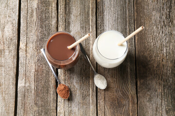 Wall Mural - Delicious protein shakes in glasses and spoons with powder on wooden table, flat lay