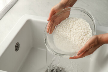 Wall Mural - Woman rinsing rice in bowl above sink, closeup