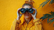 © Anatoli - Girl looking through binoculars close-up on a yellow background