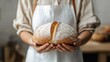 © NILSEN Studio - A baker holds a freshly baked, dusted loaf of bread with both hands, showcasing its golden crust and homey perfection against a soft-focus background.