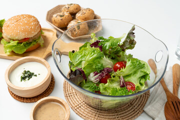 Fresh mix vegetable salad in glass blow beside dish of double meat hamburger and wholegrain bun on meal cooked by homemade serving white table. Preparing special dish menu list's restaurant. Infobahn.