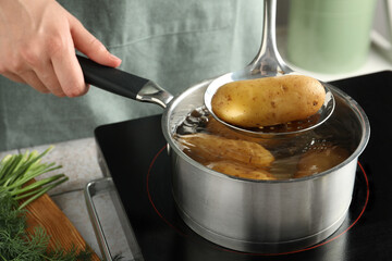 Woman taking boiled potato from saucepan on stove, closeup