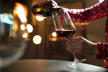 Canvas Print - Woman pouring red wine from bottle into glass at table indoors, closeup