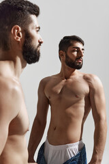 Two shirtless men with beards looking away, capturing moment of strength against warm grey background. Concept of male health, beauty and fashion, fitness, masculinity. Ad.