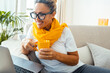 © simona - Front view of a happy adult woman working on her laptop during a video call, wearing a yellow scarf, smiling at the screen while enjoying a coffee or tea, reflecting online communication and social