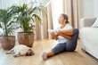 © simona - Middle age lady doing home workout in living room with sleeping dog near her. Cozy and healthy indoor leisure lifestyle. One woman in daily workout routine fit body health concept. Stretching legs