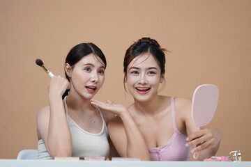 Two Asian girls aged 20-29 with Korean style makeup and hairdo, good friends, both beautiful, posing as models on a light brown background.