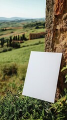 A close up center shot of a blank white 23 A4 piece of art paper leaning up against a building in the greenish fields of Tuscany