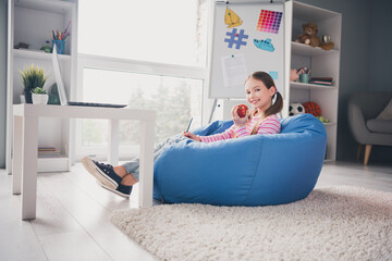 Sticker - Full body photo of cute small schoolgirl home education sit bean bag eating lunch apple school interior