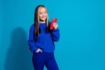 Wall Mural - Photo portrait of teenager girl in stylish knitted sweater using mobile phone blogging reading fresh post isolated on blue color background