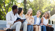 © Prostock-studio - Excited multiracial group of students discussing new educational project, sitting with laptop and notepads on stairs in park
