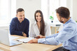 © Studio Romantic - Young couple sitting with male business broker or insurance agent showing documents sitting at the desk with laptop in office. Clients having consultation with man realtor or financial advisor.