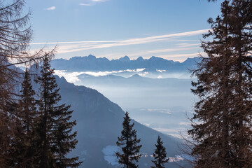 Silhouette of tree branches frame scenic view of snow capped mountain peaks of Julian Alps. Ski tour in remote alpine wilderness in Bleiberger Erzberg, Carinthia, Austria. Winter vibes Austrian Alps