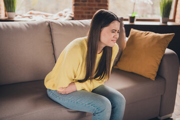 Wall Mural - Photo portrait of attractive teen woman sit sofa suffer stomach pain dressed yellow outfit cozy day light home interior living room