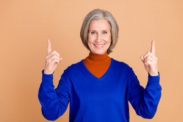 Wall Mural - Photo portrait of nice senior woman point up empty space wear trendy blue outfit isolated on beige color background