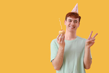 Poster - Young man with birthday tartlet showing victory gesture on yellow background