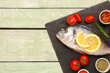 Poster - Slate board of raw dorado fish with lemon, tomatoes and spices on green wooden background