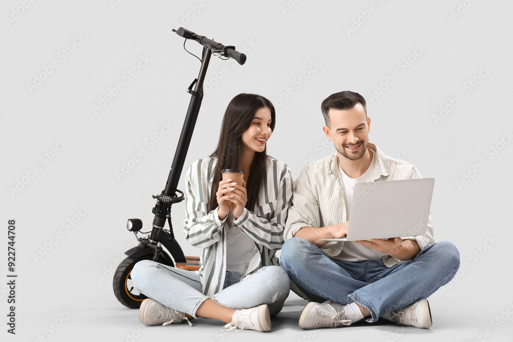Young couple with coffee cup, laptop and electric scooter on light background