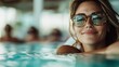 ©  lukaPixMedia - A woman wearing sunglasses smiles in a swimming pool, exuding relaxation, happiness, and the carefree enjoyment of vacation and leisure time.