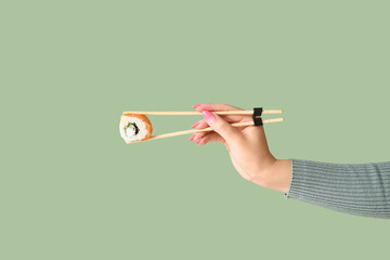 Wall Mural - Female hand holding tasty sushi roll with chopsticks on green background