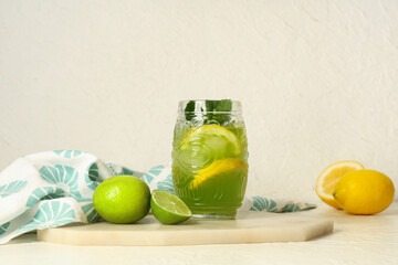 Wall Mural - Board with glass of tasty lemonade, lemons, limes and mint on white background