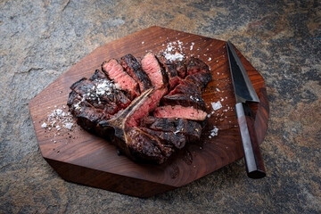 Wall Mural - Traditional barbecue dry aged wagyu porterhouse beef steak bistecca alla Fiorentina sliced with salt and pepper served as close-up on a wooden design board with a Japanese knife