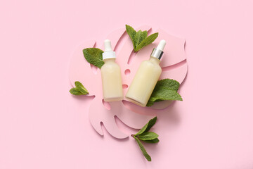 Wall Mural - Bottles of essential oil, plaster palm leaf and mint leaves on pink background