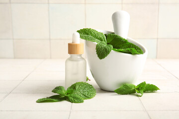 Wall Mural - Bottle of essential oil, mortar, pestle and mint leaves on tile background, closeup