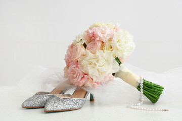 Beautiful wedding bouquet, shoes and bride's veil on light background