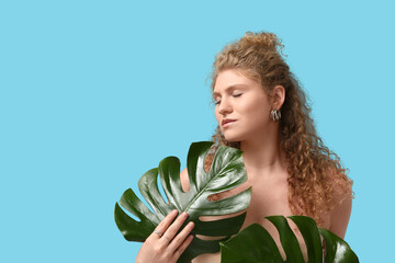 Wall Mural - Beautiful young woman with tropical monstera leaves on blue background