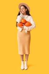 Wall Mural - Stylish young woman with fresh pumpkins on yellow background