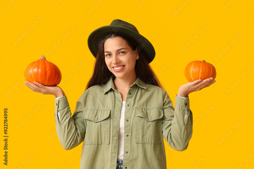 Stylish young woman with fresh pumpkins on yellow background