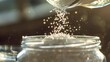 © buraratn - A close-up of salt being poured into a glass jar, with granules cascading down, symbolizing preservation and flavor.