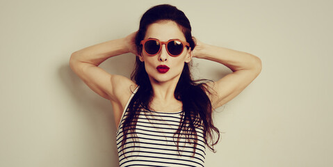 Wall Mural - Fun relax smiling woman posing in fashion sunglasses and stripped t-shirt with red lipstick on studio wall background with empty copy space. Fashion lifestyle portrait. Toned