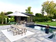 © theplantedwanderer - High-end outdoor living space, a backyard patio with pergola, outdoor rug,  tequila bar, dining set, couch, television, pool with waterfall, umbrella, fire pit and stunning grey patio. Modern vibe.