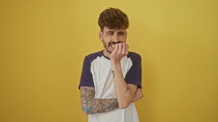 Canvas Print - Young hispanic man; an image of anxiety and stress over isolated yellow background, nervously standing, stressed, fearing, biting hands and looking seriously troubled