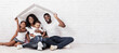 © Prostock-studio - Family Housing Concept. Young African American Parents With Two Children Sitting Under Cartboard Roof Dreaming Of New Home, Copy Space