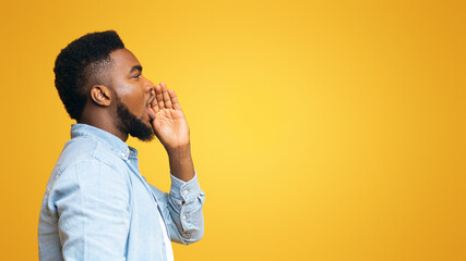 profile portrait of black guy making announcement, shouting at copy space on yellow studio backgroun