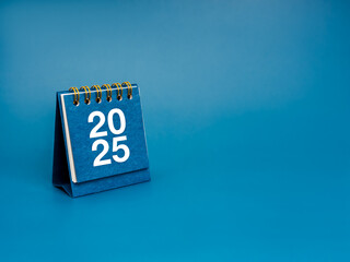 Poster - happy new year 2025 background. white 2025 number on small desk calendar cover standing on blue back