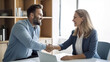 © halo - A photo of an office worker shaking hands with his female boss in front of her desk, both smiling and looking at each other.