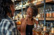 © lenblr - Liquor store owner smiling and helping a customer choosing a bottle of alcohol, she is holding a bottle and talking with her