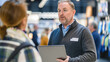 © lenblr - Professional salesman with laptop talks to customer at trade show, showcasing business communication and technology in retail setting. Background is blurred, hinting at busy atmosphere of event