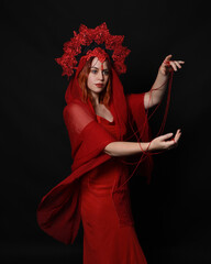 Wall Mural - close up portrait of beautiful female model wearing an ornate gothic fantasy crown and red dress. knotted string wrapped around arms, hands holding entwined rope. isolated on dark studio background.