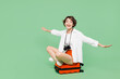 © ViDi Studio - Full body smiling happy traveler woman wear casual clothes sit on suitcase bag spread hands pov fly isolated on plain green background Tourist travel abroad in free time rest. Air flight trip concept