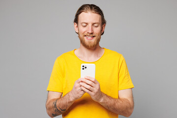 Poster - Young smiling happy man he wears yellow t-shirt casual clothes hold in hand use mobile cell phone chatting online surfing internet isolated on plain grey background studio portrait. Lifestyle concept.