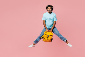 Wall Mural - Full body young shocked surprised fun Indian boy student wear blue t-shirt casual clothes hold in hand backpack bag jump high isolated on plain pink background. High school university college concept.