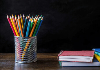 Poster - Back to school concept with colorful pencils and books on desk with a blackboard background